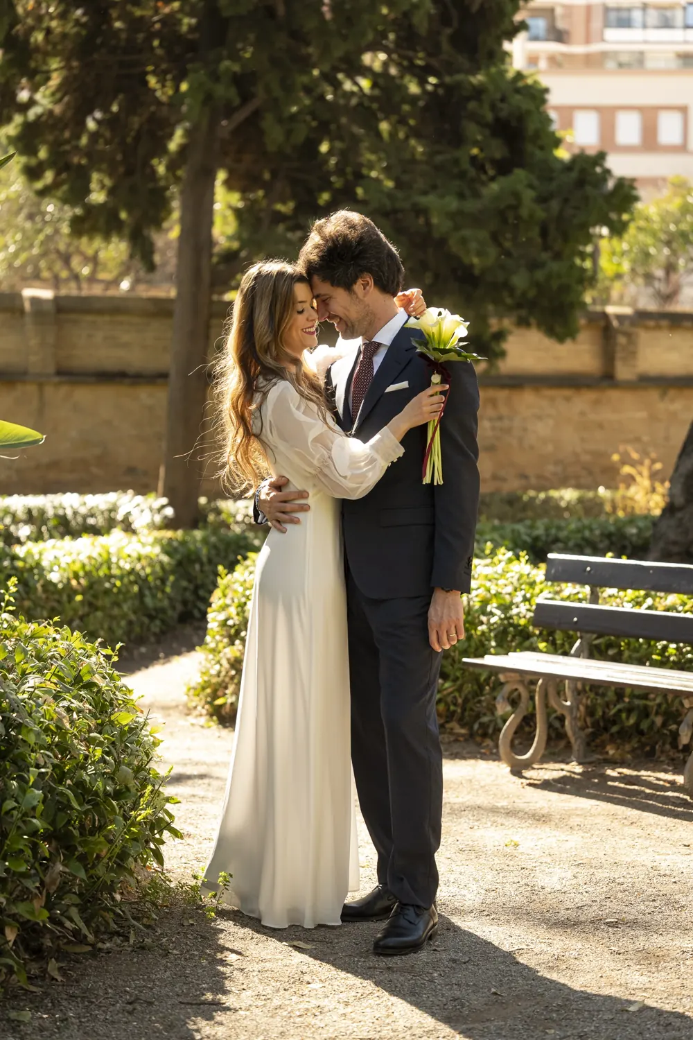 Los novios abrazados en un jardín al sol