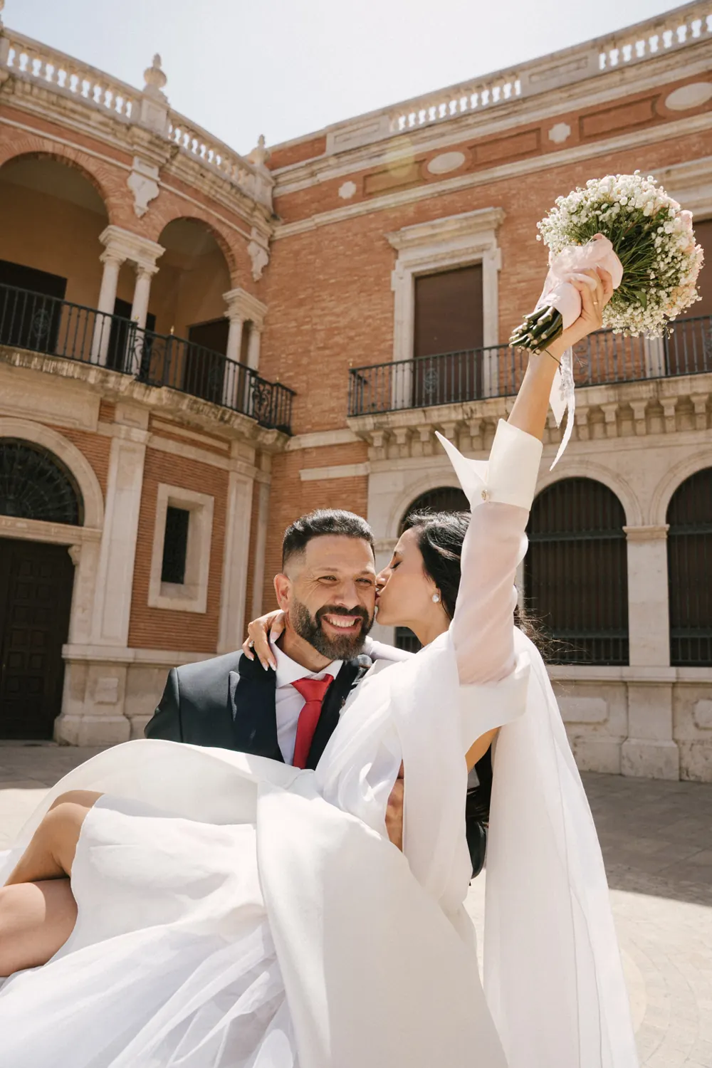 La novia besa al novio mientras él la sostiene en brazos