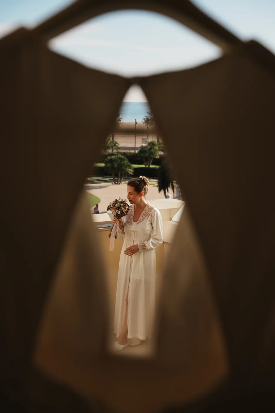 La novia huele el ramo en el balcón, vista a través de una abertura